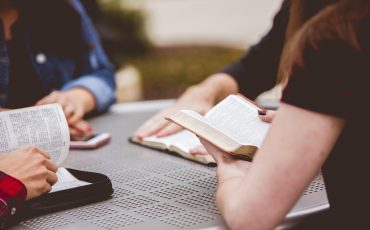 Closeup shot of females sitting around the table reading the bible with a blurred background