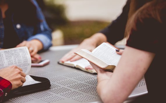 Closeup shot of females sitting around the table reading the bible with a blurred background