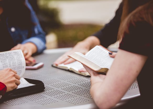 Closeup shot of females sitting around the table reading the bible with a blurred background
